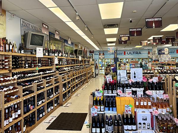 A long aisle of wooden wine racks stretching to the back of the shop, with overhead signs marking each region.